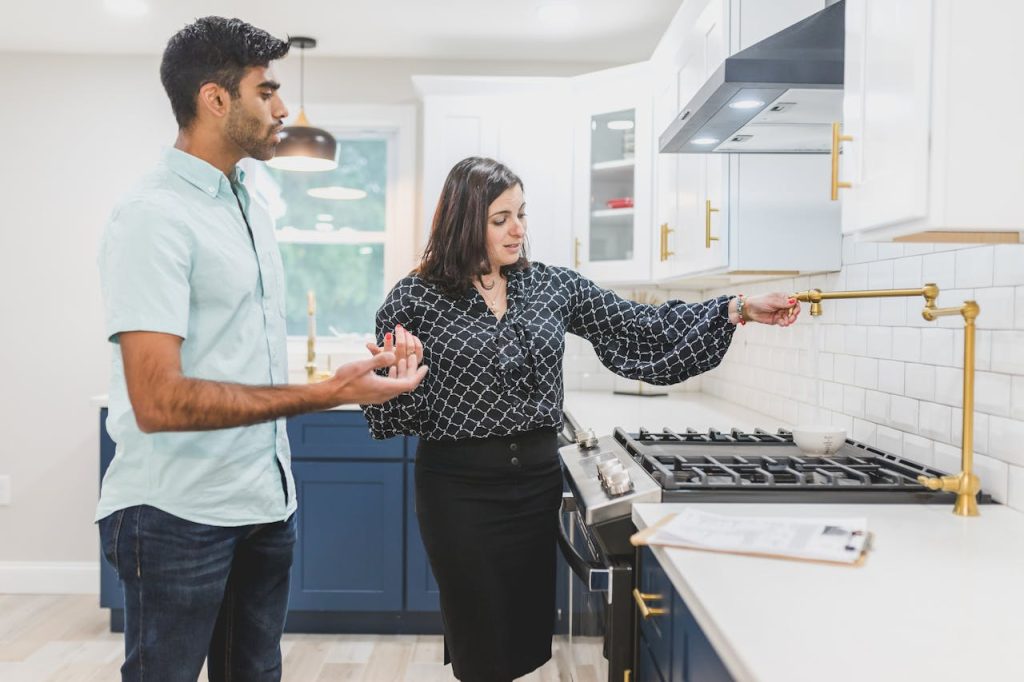 Real estate agent showing a modern kitchen interior with brass fixtures to a client.